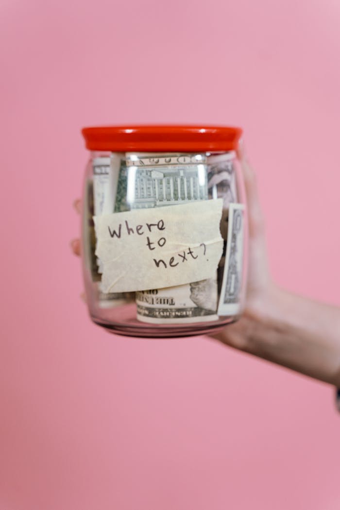 A jar filled with cash and a travel note against a pink backdrop symbolizing savings.